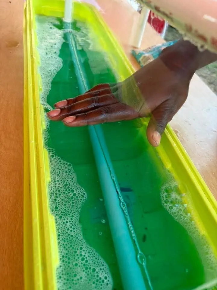 A hand tests water displacement in a bright green trough at a Brainstorms popup