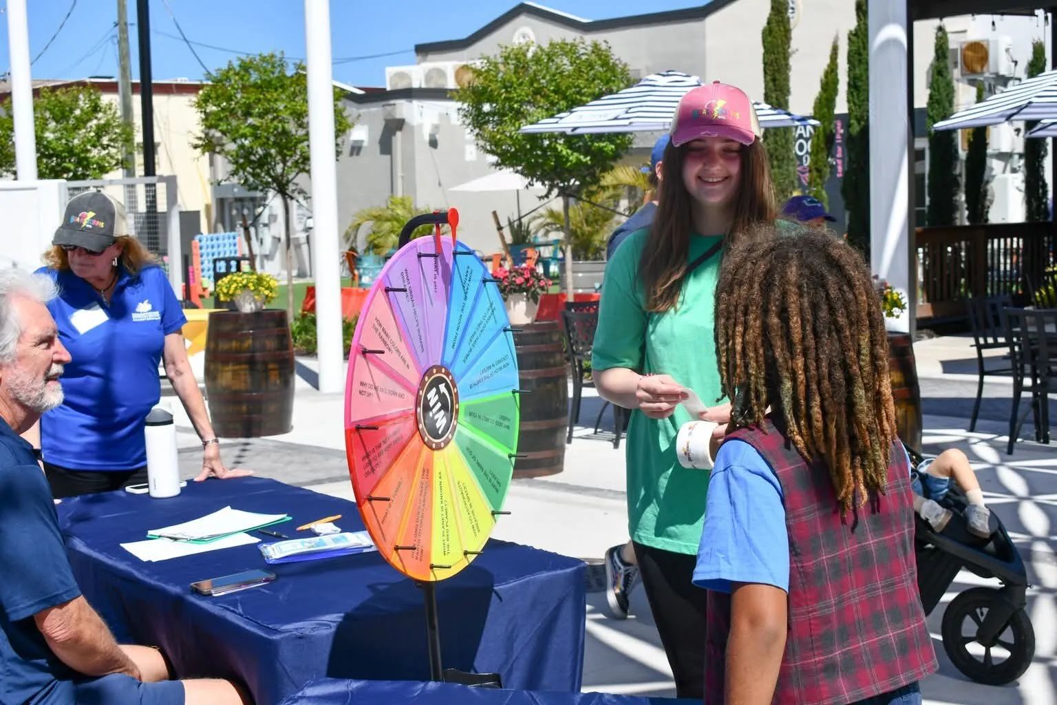 Brainstorms volunteers greet a young visitor at a prize wheel during an outdoor community event